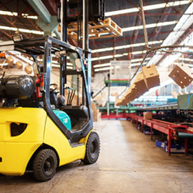 The forklift is in a large and light warehouse. Yellow color.