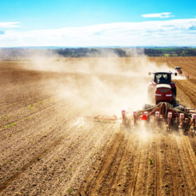 Aerial view of the the tractor harrowing the large brown field in spring season