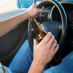 Car driver is holding a bottle of beer in his hand