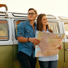 Tourist Man And Woman With Map In Nature Near Car. Happy Man And Beautiful Smiling Woman Using Map While Traveling On Summer Weekend Outdoors. Couple Travel On Sunny Day. High Quality Image.