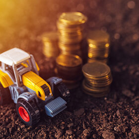 Agricultural tractor toy and golden coins on fertile soil land, income from activity in agriculture or investment and bank loans for farm development
