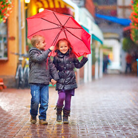 happy kids walking under the rain on colorful street
