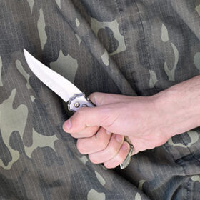 Hand with small knife on camouflage fabric background. The concept of using a knife in melee tactics among the military