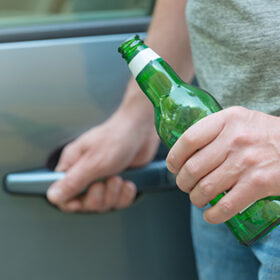 Man opening his car while holding a bottle of beer. Don't drink and drive concept