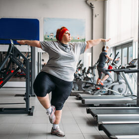 Fat woman doing balance exercise in gym. Calories burning, obese female person on workout in sport club