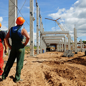 two builder workers at construction site during concrete pole and beam installation