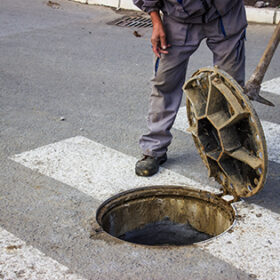 utilities worker moves the manhole cover to check the sewer line for clogs