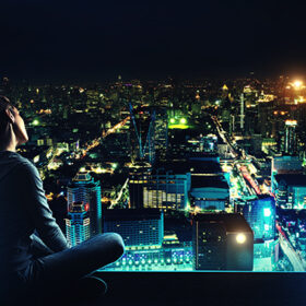 Pensive woman is sitting on the roof and looking at night city