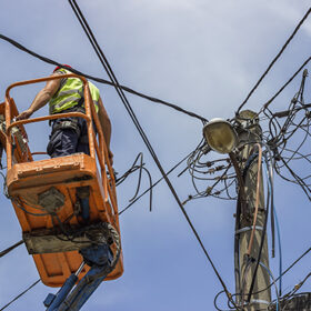Utility pole worker installs new cables on an electric pole from lift bucket.