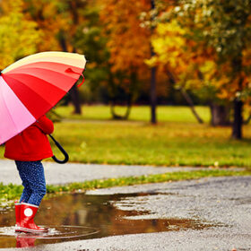 happy child girl with umbrella walking through the puddles after autumn rain
