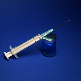 Vaccine bottle phial with no label, medical syringe injection needle. isolated on blue background. Development of coronavirus vaccine COVID-19. cure. World race in researching. copy space