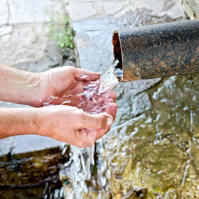 Spring water flows from the pipe into the hands of the men on the background of stone