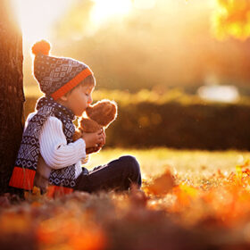 Adorable little boy with teddy bear in the park on an autumn day in the afternoon, sitting on the grass