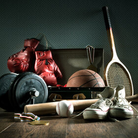 Teenager sport equipment in a vintage suitcase including sports footwear, boxing gloves, weights and baseball bat.