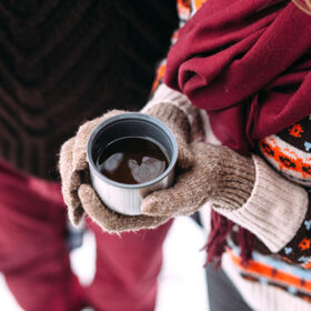woman hands pours hot tea or coffee out of thermos on winter forest background. girl using a thermos on a snowy day. metallic cup