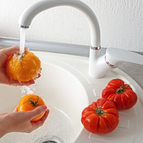 Female hands washing tomatoes in kitchen sink