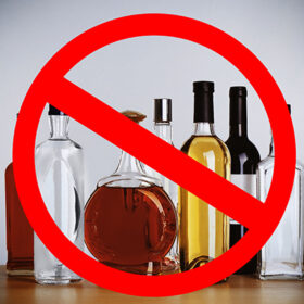 Different alcohol drinks in bottles with STOP sign on grey background