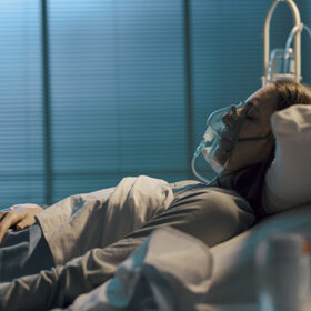 Woman with oxygen mask lying in a hospital bed at night, medicine and healthcare concept