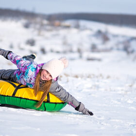 Young girl outstretched her arms while enjoying snow tubing at sunny winter weather