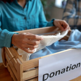 Sorting clothes. Female hands taking a sweater out of a wooden box of sortable clothes, holding a beige sweater.