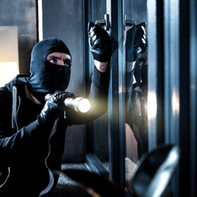 Burglary. Skilful professional masked burglar opening a window and holding a torch and breaking into the house