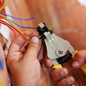 Electrician peeling off insulation from wires - closeup on hands and pliers