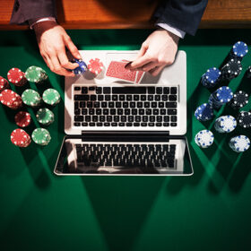Man playing online poker with laptop on a green table with chips all around top view, he is looking at his cards