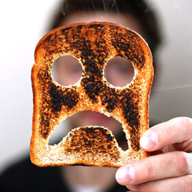 Man holding up a burnt slice of toast with an unhappy smiley conept for bad start to the day