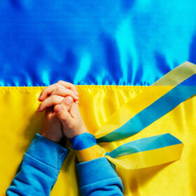 Kids hands with ribbon praying on the Ukrainian flag background. Symbol of peace and pray for Ukraine. Top view, flat lay. Selective focus on the hands.